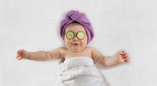 Funny baby girl wrapped in white towel with cucumbers on her eye