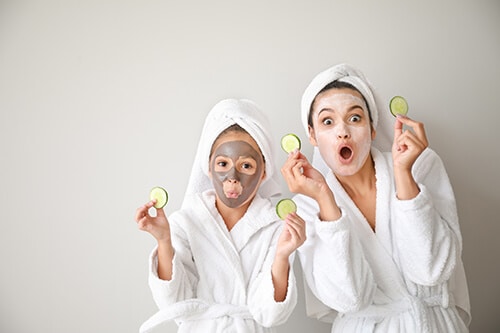 Funny mother and her little daughter with facial masks and cucum